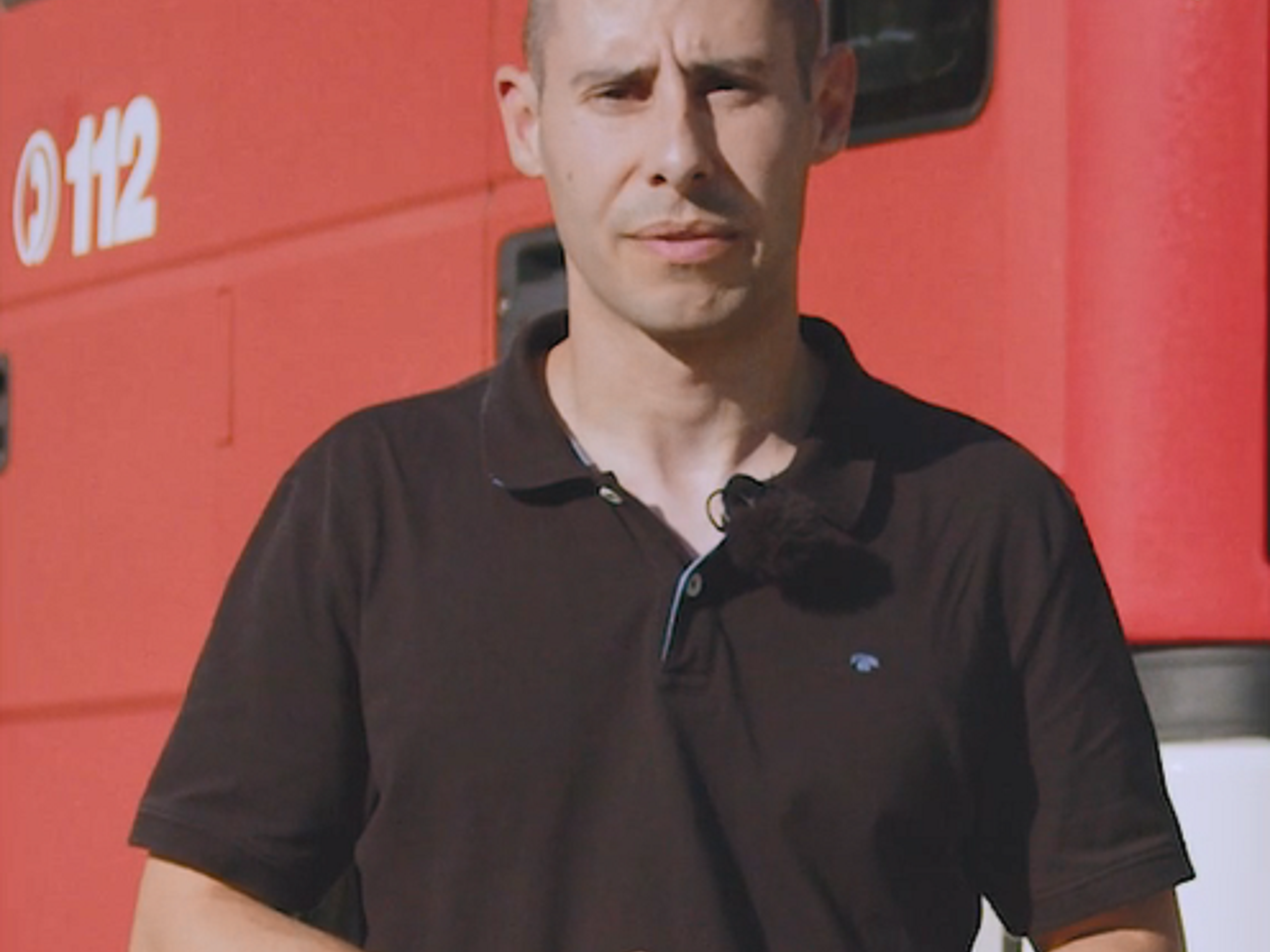 Mann in schwarzem Polohemd vor rotem Auto